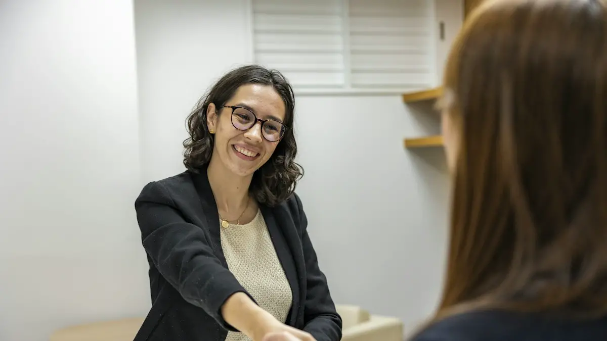 A woman shaking hands with another woman sitting at a table.
