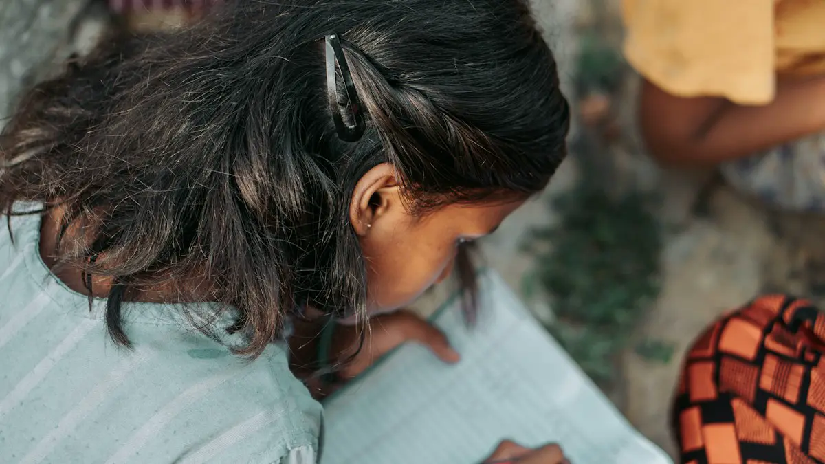 Young girl writing in a notebook with a pencil.