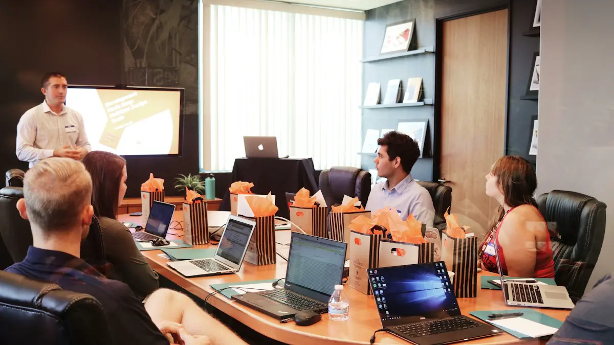 Man standing in front of people sitting beside table with laptop computers.