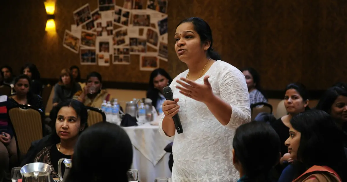 A young woman speaking into a microphone in front of a group.