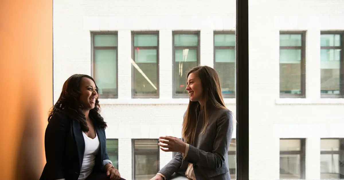 Two colleagues in conversation by an office window.
