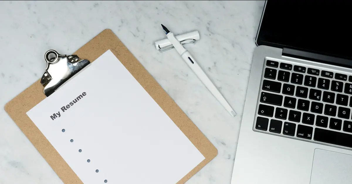 A resume on a clipboard beside a laptop.