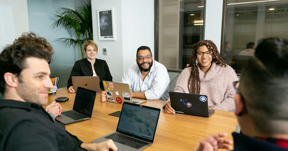 A team meeting around a table with laptops.