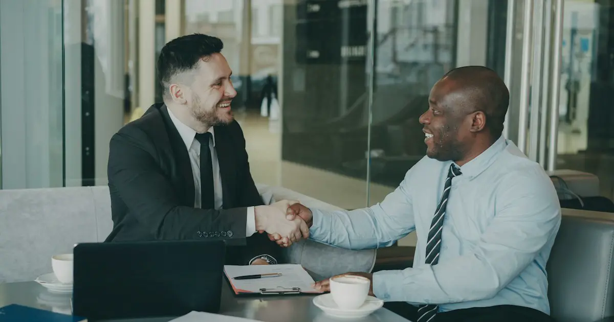 Two people shaking hands across a desk after an interview.