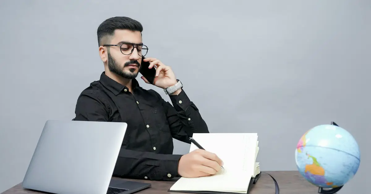A candidate on a phone call, taking notes beside a laptop.