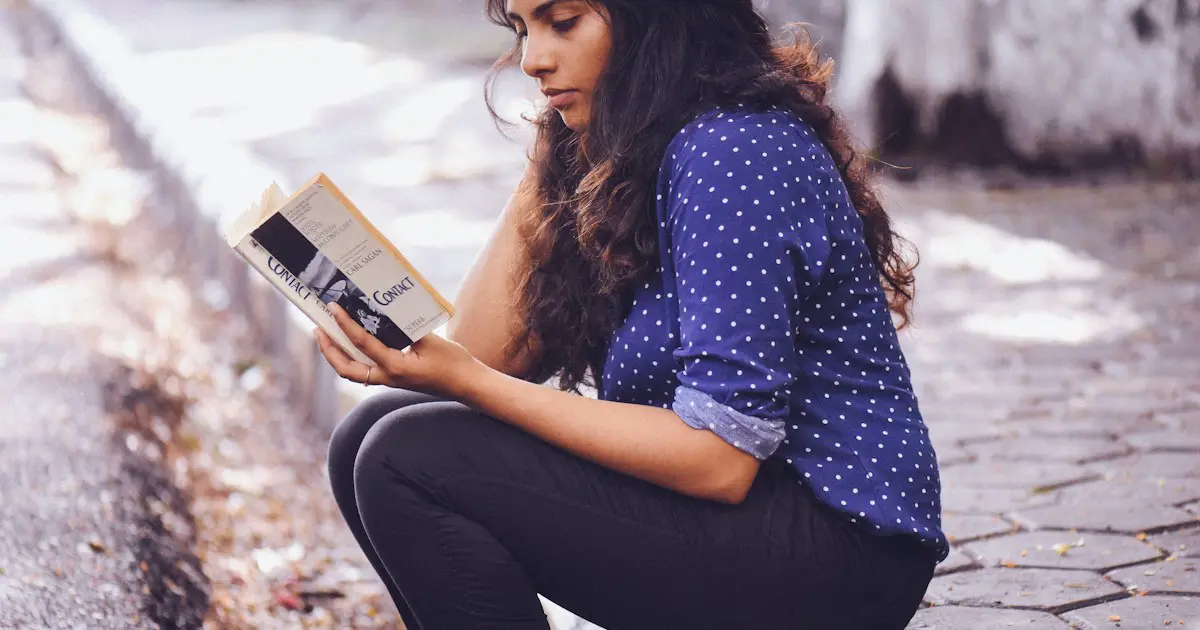 A young woman reading a book on some steps.